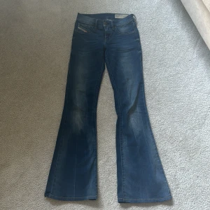 Blå bootcut jeans från Diesel - Säljer ett par blå bootcut jeans från Diesel, modell Larkee-Flare. Jeansen har låg midja, klassisk femficksdesign och snygga slitningar framtill. Stretchigt material för extra komfort. Perfekta för dig som gillar en retroinspirerad look.