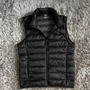 Svart dunväst från Uniqlo - Säljer en svart, ultra light dunväst från Uniqlo. Västen har hög krage och dragkedja framtill. Perfekt för lager-på-lager och enkel att bära tack vare sin lätta design. Stilren väst och passar till allt. Storlek xxs men passar också xs. 10/10 skick inga synliga defekter alls.