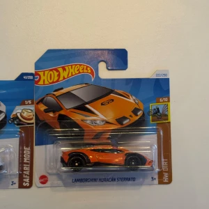 Hot Wheels Lamborghini Huracán Sterrato. Offroad special - Två Hot Wheels-bilar, Lamborghini Huracán Sterrato, en i orange med svarta detaljer och en i vitt med svarta och orange detaljer. Båda är i originalförpackning och har sportig design med tydliga linjer. 