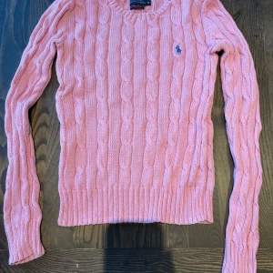 Rosa kabelstickad tröja från Polo Ralph Lauren - Säljer en klassisk rosa kabelstickad tröja från Polo Ralph Lauren med blå broderad logga på bröstet. Den är i fint skick! Nypris var 1800kr. Knappt nånsin använt. Skriv till mig om ni har några frågor!