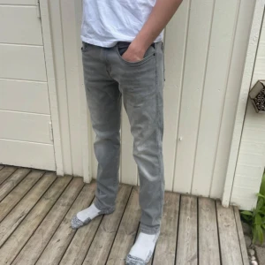 Grå jeansbyxor från Replay - Säljer ett par grå jeansbyxor från Replay med raka ben och klassisk femficksdesign. Byxorna har diskreta sömdetaljer på bakfickorna och normal passform. Perfekta för en stilren och avslappnad look.