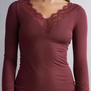 Röd intimissimi spetstopp  - Säljer en vinröd långärmad topp från intimissimi med djup v-ringning och fina spetsdetaljer runt halsen. Toppen är figurnära och passar perfekt till många olika outfits. Materialet är mjukt och stretchigt för en bekväm känsla. Storlek S, aldrig använd. Köp gärna via köp nu knappen❤️