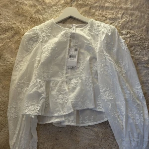 Vit blus med broderade blommor från Mango - Säljer en vit blus från Mango i storlek XS. Blusen har lång ärm, rund halsringning och är dekorerad med broderade blommor. Kostar 599kr nypris. 