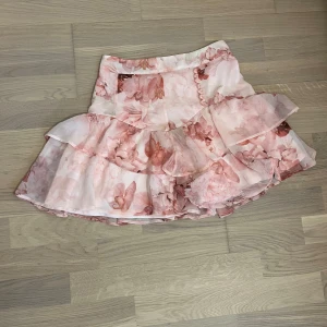 Rosa blommig volangkjol från Mohito - Supersöt kjol från Mohito i ljusrosa med blommigt mönster och volanger. Kjolen har omlottkänsla och fina detaljer längs kanten. 