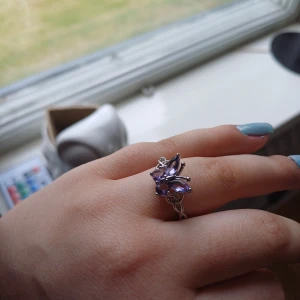 Silverring med lila stenar i blomform - Unik silverring med flera lila stenar formade som blomblad. Ringen har en elegant och detaljrik design som verkligen sticker ut. Perfekt för dig som vill ha något speciellt på fingret.