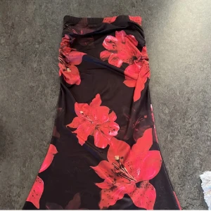 Svart långkjol med stora röda blommor - Snygg svart långkjol med stora röda blommor. Kjolen har en åtsittande passform upptill och vidgar sig nedåt. Perfekt för en färgstark look! Säljer pga har en exakt likadan redan så denna är helt ny!! ❤️