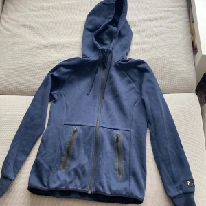 Blå hoodie från Peak Performance - Säljer en blå hoodie från Peak Performance i storlek S. Tröjan har dragkedja framtill, två fickor med dragkedja och huva med dragsko. Perfekt för kyliga dagar eller till träning. (För små för mig)