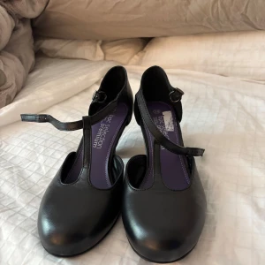 Svarta ballerinaskor med rem - Säljer ett par svarta ballerinaskor med rund tå och justerbar rem runt vristen. Skorna har en klassisk design och är tillverkade i ett slätt material. Säljer för råkade köpa för storlek. Passar bra till dans🥰