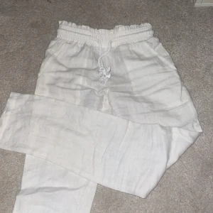 Vita linnebyxor med snörning - Säljer ett par fräscha vita linnebyxor med elastisk midja och snörning. Byxorna har avslappnad passform och är perfekta för varma dagar. Lätta och luftiga med raka ben och fickor på sidorna.