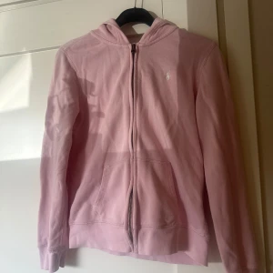 Rosa hoodie från Polo Ralph Lauren - Säljer en ljusrosa hoodie från Polo Ralph Lauren med dragkedja och huva. Tröjan har fickor framtill och en liten broderad logga på bröstet. Perfekt för en avslappnad stil. Storlek 16 passar mig som har s/xs