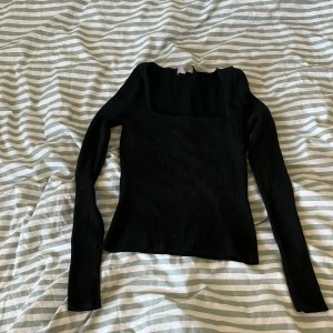Svart ribbad långärmad topp från H&M - Säljer en svart ribbad långärmad topp från H&M med fyrkantig ringning. Toppen är tight och har en stilren design som passar perfekt till många olika outfits.