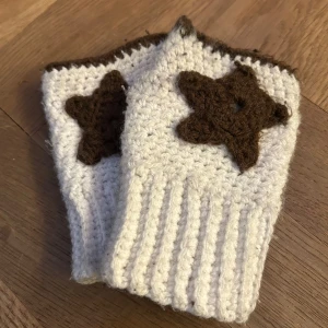 Stickade vita handvärmare med bruna stjärnor - Stickade vita handvärmare med bruna stjärnor på ovansidan och bruna kanter upptill. De är ribbstickade vid handleden och har öppning för tummen. Perfekta för kyliga dagar.