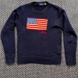 Mörkblå stickad tröja från Polo Ralph Lauren - Säljer en mörkblå stickad tröja från Polo Ralph Lauren med amerikansk flagga och RL-broderi framtill. Tröjan har rund halsringning och långa ärmar. Tröjan är otroligt eftertraktad och har ett nypris värde på 6000-8000! Hör av er vid minsta lilla fråga 
