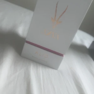 ALID Extrait de Parfum - Lyxig parfymflaska från ALID med gulddetaljer och en elegant lila-rosa glasflaska. Förpackningen är vit med guldtext och en stilren illustration av ett djurhuvud. Parfymen är en Extrait de Parfum vilket innebär hög koncentration av doft.