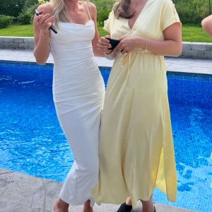 Vit långklänning med slits från Zara - Säljer en elegant vit långklänning från Zara i storlek XS. Klänningen har smala axelband, figurnära passform och en snygg slits framtill. Materialet är mjukt och lätt, perfekt för sommarens tillfällen. Varan har en lite fläck från ett ljusrosa läppglans ( se bild) men det är inget man tänker på när man har på sig den. Går säkert bort i tvätten. 