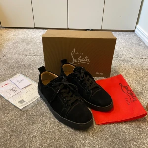 Svarta Louboutins - Säljer ett par svarta sneakers från Christian Louboutin med klassisk röd sula. Skorna är i mocka med svarta snören och har en rund tå. Innersulan är beige och märkt med Louboutin Paris. Kommer med originalkartong och dustbag.
