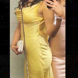 Gul långklänning i satin - Säljer en elegant gul långklänning i satin med draperad urringning och figurnära passform. Klänningen har smala axelband och en mjukt glansig yta som ger en lyxig känsla. Perfekt för speciella tillfällen. BAL!!!!!!!