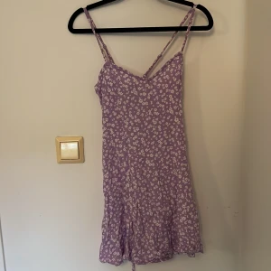 Ljuslila blommig klänning från FB Sister - Supersöt ljuslila klänning från FB Sister med vita småblommor. Klänningen har smala axelband, snörning i ryggen och en lätt volang nertill. Perfekt för varma dagar och ger en romantisk vibe.