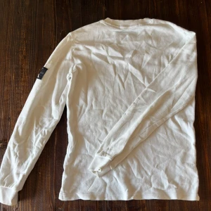 Vit långärmad tröja från Calvin Klein - Säljer en vit långärmad tröja från Calvin Klein med logga på ena ärmen. Tröjan har rund halsringning och är tillverkad i ett mjukt material som passar perfekt till vardags. Enkel och stilren design.