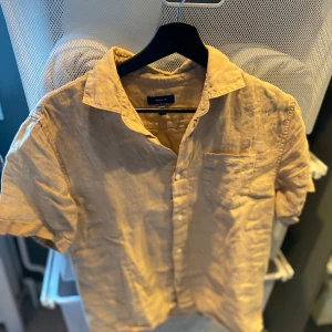 Gant linneskjorta - Säljer en beige kortärmad skjorta från GANT i linne.  Bara använd ett fåtal gånger.                                    Storlek 158-164cm eller 13-14 år                                       Köpt ifrån NK för ungefär 1 år sedan                                   Ordinarie pris är 1000kr