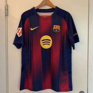 FC Barcelona hemmatröja Raphinha  25/26 - Säljer en officiell FC Barcelona fotbollströja med Raphinha 11 på ryggen. Tröjan är blå och röd med gula detaljer, Nike-logga och Spotify som sponsor. Kortärmad modell i ventilerande material, perfekt för match eller träning.