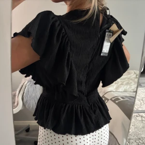 Svart blus med volang från vero moda - Supersnygg svart blus från vero moda med volangdetaljer längs ärmar och nederkant. Storlek M men väldigt liten så som en S. Köpt för 349kr prislappen är på