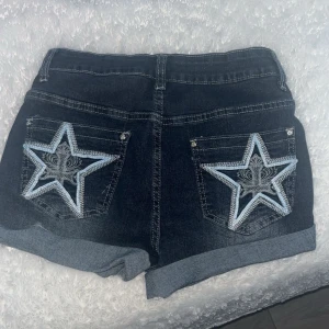 Mörkblå jeansshorts med stjärndetalj - FINNS OCKSÅ I (S,36)!! Snygga mörkblå jeansshorts med uppvikta ben och stora broderade stjärnor i vitt och ljusblått på bakfickorna. Perfekta för sommardagar och ger en cool look med sin unika detalj på fickorna.❤️