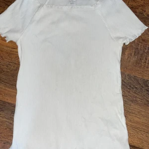 Vit ribbad topp med kort ärm - Säljer en enkel och stilren vit ribbad topp med korta ärmar och rund halsringning. Perfekt att matcha med jeans eller kjol för en clean look. Väldigt Stretchig