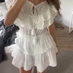 Vit klänning med volanger - Charmig vit klänning med volanger och kort ärm. Den har en smickrande v-ringning och elastisk midja för en bekväm passform. Perfekt för sommarens alla tillfällen. ☺️Är storlek S/M men sitter bra på mig som brukar ha S. Passar till studenten också! ☀️