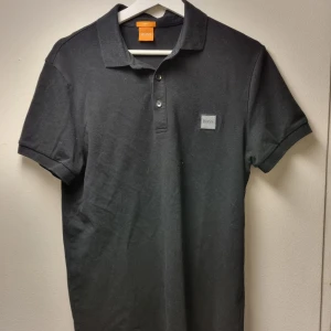 Svart pikétröja från BOSS - Klassisk svart pikétröja från BOSS med krage och två knappar framtill. Slim fit-modell i mjukt material.  Nypris: ca 949 kr