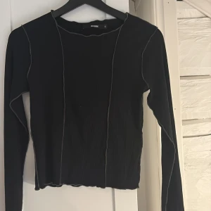 Svart ribbad långärmad topp från BikBok - Svart långärmad topp från BikBok med ribbad struktur och synliga sömmar i kontrastfärg. Modellen är croppad och har en rå kant vid halsen för en trendig look. Perfekt till jeans eller kjol. Hör av er vid intresse!💕