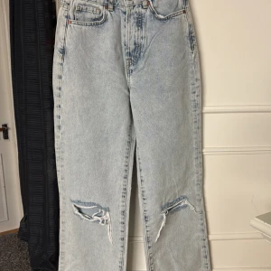 Ljusblå slitna jeans med raka ben - Ljusblå jeans från Never Denim med hög midja och raka ben. Jeansen har slitningar på båda knäna och klassisk femficksdesign. Perfekta för en avslappnad och trendig look.