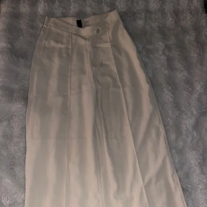 Beiga vida kostymbyxor  - Stilrena beiga kostymbyxor från SHEIN med hög midja och vida ben. Byxorna har klassisk knapp- och dragkedjestängning framtill och är perfekta för en trendig look. Materialet känns mjukt och lätt, vilket gör dem bekväma att bära hela dagen.