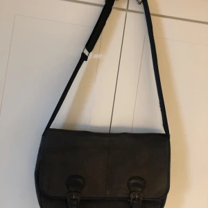 Brun axelväska - Säljer en stilren brun axelväska med justerbar axelrem. Väskan har ett klassiskt lock med två spännen framtill och magnetlås. Perfekt för att bära med sig det viktigaste till skolan eller stan.