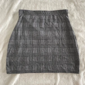 Rutig kortkjol från Vero Moda - Säljer en snygg kortkjol från Vero Moda i svart och grått med klassiskt rutigt mönster. Kjolen har en rak passform och är perfekt för dig som gillar stilrena plagg med lite edge. Superenkel att matcha med både stickade tröjor och t-shirts. 