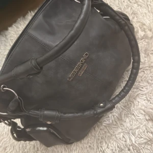 Svart axelväska från Liebeskind - Säljer en svart axelväska från Liebeskind med silverfärgade metalldetaljer och dragkedjor. Väskan har två rejäla handtag och en praktisk ytterficka med dragkedja. Perfekt för dig som vill ha en stilren och rymlig väska till vardagen.