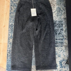 Ash grey alpaca byxor från Our Legacy - Mörkgrå, fluffiga byxor från Our Legacy i modellen Reduced Trousers. Tillverkade i en mjuk och lyxig alpackablandning med rak passform och elastisk midja. Perfekta för dig som vill ha något unikt och bekvämt.