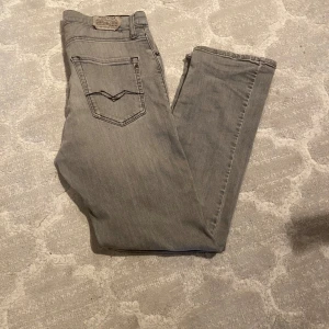 Grå jeansbyxor från Replay 29w/32L - Säljer ett par grå jeansbyxor från Replay med klassisk femficksdesign och raka ben. Byxorna har snygga detaljer på bakfickorna och en diskret logga på linningen. Perfekta för en stilren och avslappnad look.