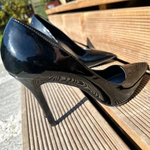 Svarta lackade pumps  - Säljer ett par klassiska svarta pumps med klack och spetsig tå. Skorna är i glansigt syntetmaterial och har en elegant och tidlös design som passar till många olika outfits.