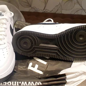 Nike Air Force 1 vita och svarta sneakers - Säljer ett par klassiska Nike Air Force 1 sneakers i vitt med svarta detaljer, skit feta nu till sommaren!