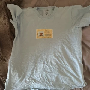 Ljusblå t-shirt Call Me If You Get Lost konsert tröja  - Ljusblå t-shirt med tryck framtill som liknar ett resedokument och texten 'Call Me If You Get Lost'. 100% bomull och medium fit. Perfekt för dig som gillar unika och kreativa plagg.