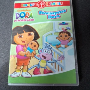 Storasyster Dora - DVD med Dora Utforskaren: Storasyster Dora. Innehåller fyra avsnitt där Dora och hennes vänner är med om olika äventyr. Färgglad framsida med Dora, Boots och en bebis. Svenskt tal, del av Barnens Favoriter-serien. Bra skick