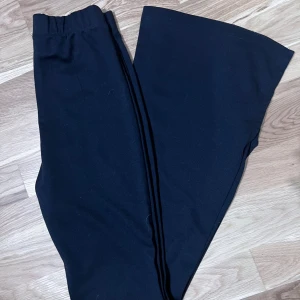 Svarta bootcut byxor - Svarta bootcut byxor med resår i midjan. Byxorna har en mjuk och stretchig känsla, perfekt för en avslappnad stil. Passformen är normal upptill och blir vidare nedtill för en snygg siluett.