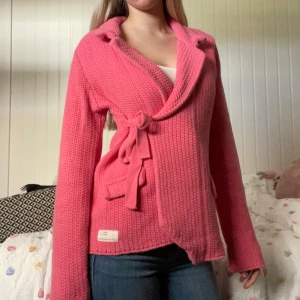 Odd Molly tröja - Säljer en rosa stickad cardigan jacka med bred krage och knytband i midjan. Jackan har två fickor framtill och en mjuk, grovstickad struktur. Perfekt för dig som vill ha en mysig look i en snygg färg som passar perfekt till sommaren. Från odd Molly, strl 3 men skulle säga att den passar S/M