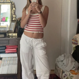 Vit och röd randig stickad linnetopp - Säljer en söt stickad linnetopp med breda röda och vita ränder. Toppen är ärmlös och har en croppad passform, perfekt för varma dagar. Enkel och stilren design som passar till mycket.