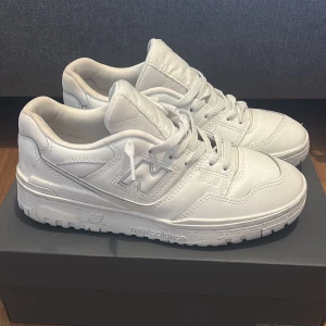 Vita sneakers från New Balance - Snygga vita sneakers från New Balance med klassisk design och snörning. Skorna har en robust sula och är perfekta för en stilren look. Passar bra till både jeans och shorts. Har storlek 39.