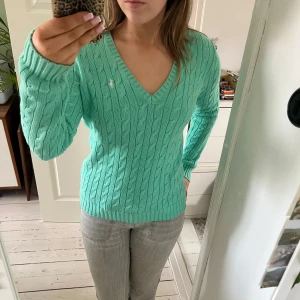 Mintgrön stickad tröja från Ralph Lauren - Säljer en snygg mintgrön stickad tröja från Ralph Lauren med kabelstickat mönster och v-ringning. Tröjan har långa ärmar och en liten logga på bröstet. Perfekt för en stilren look! 💚Jag har vanligtvis storlek S men denna tröjan sitter bra men lite löst på mig och den är storlek M. PRISET GÅR ATT PRUTA!