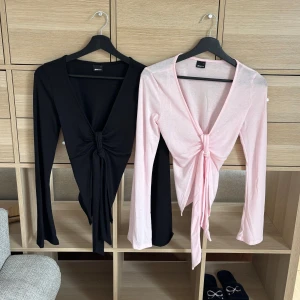 Toppar från Gina Tricot (2-pack) - Två långärmade toppar i svart och rosa med knyt framtill. Båda topparna ingår i priset. Topparna är helt oanvända och har bara stått i garderoben.