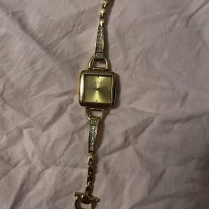 Elegant guldfärgad klocka från regal med fyrkantig urtavla och gnistrande detaljer på armbandet. Perfekt för att lägga till en touch av lyx till din stil. 19mmx19mm