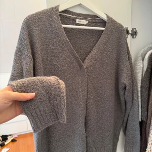 Grå kofta  - Mysig grå kofta med v-ringning och långa ärmar. Perfekt för kyliga dagar, den har en mjuk och bekväm textur. Ett stilrent plagg som passar till många olika outfits.